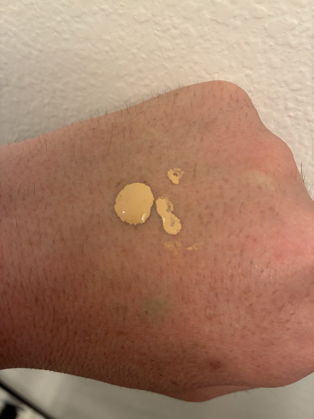 Back of hand showing a small dot of liquid foundation — roughly a quarter pump dispensed ready for brush application